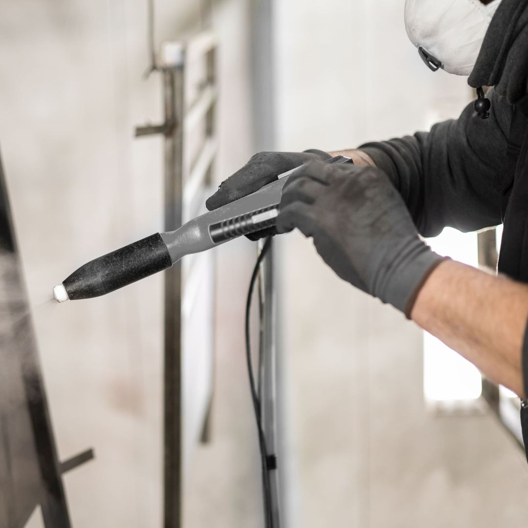 Ein Mann mit Maske und Handschuhen benutzt eine Spritzpistole für präzise Arbeiten.